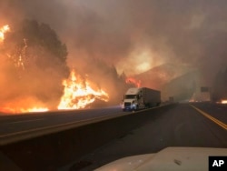 In this Sept. 5, 2018, photo released by the U.S. Forest Service, a truck drives next to the Delta Fire burning on Interstate 5 near Shasta-Trinity National Forest, Calif.