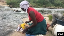For Chipo Masvinga, the right to water in Zimbabwe’s constitution since 2013 is still far away, with infant daughter Esther and 4-year-old son Emmanuel, she does laundry in Mukuvisi river in Harare, March, 2017. (C. Mavhunga/VOA)