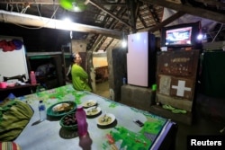 FILE - A woman watches TV as seawater hits her house during high tide in Sriwulan village in Demak, Indonesia, Jan. 31, 2018.
