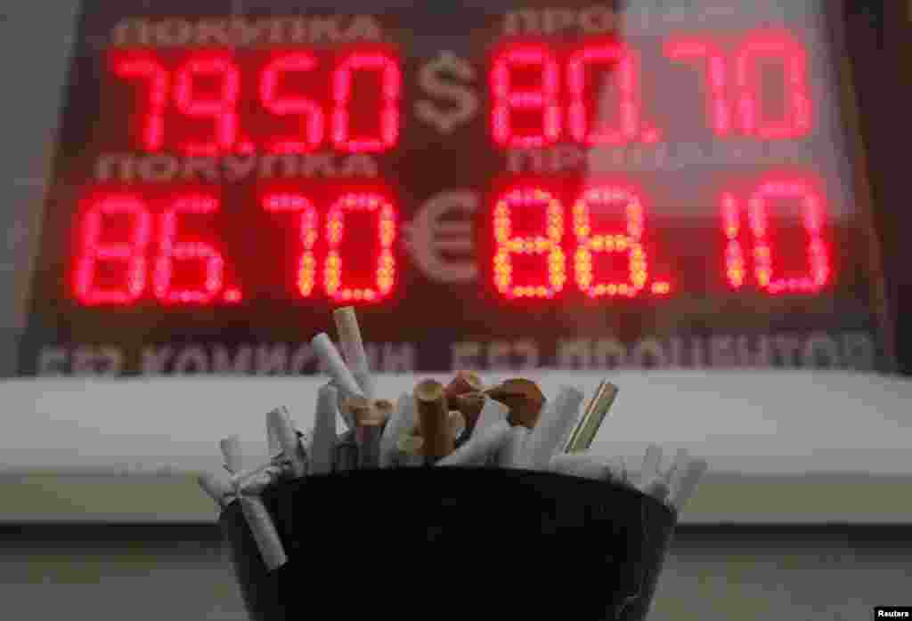 An ashtray filled with cigarette butts in front of a board showing currency exchange rates of the U.S. dollar and euro against the ruble in Moscow, Russia.&nbsp;The Russian ruble weakened to a new record low against the dollar on Wednesday as the mood on global markets was torrid and oil prices slumped.&nbsp;
