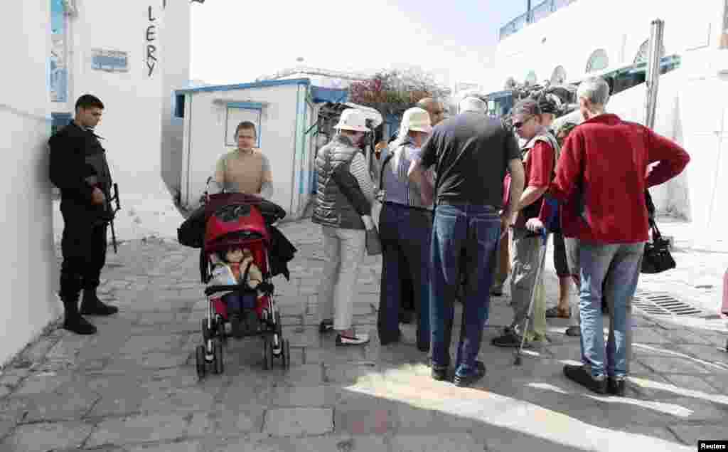 A police officer stands guard as tourists walk in Sidi Bou Said, a tourist destination, in Tunis, March 23, 2015.