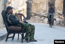 FILE - A Free Syrian Army fighter sits at a checkpoint as a man rides a bicycle past the rubble of a damaged building in the old city of Aleppo, Syria, July 13, 2015.