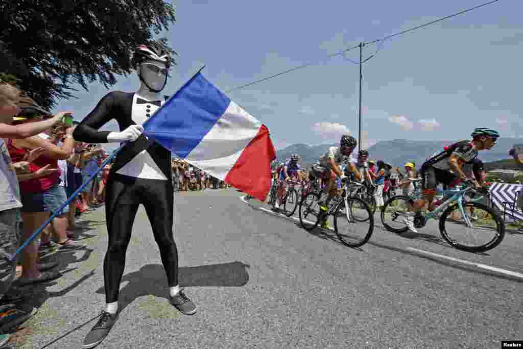 The pack of riders cycles past a French flag on Bastille day during the 242.5 km fifteenth stage of the centenary Tour de France cycling race from Givors to Mont Ventoux, July 14, 2013. 