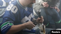 FILE - A man is seen smoking marijuana prior to last year's Super Bowl. A new study says college students are choosing marijuana over tobacco.