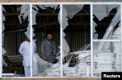Afghan men look outside a broken window at the site of a suicide attack in Kabul, Afghanistan, Sept. 9, 2018.