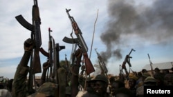 FILE - Rebel fighters hold up their rifles as they walk in front of a bushfire in a rebel-controlled territory in Upper Nile state, South Sudan Feb. 13, 2014. 