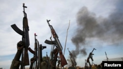 FILE - Rebel fighters hold up their rifles as they walk in front of a bushfire in a rebel-controlled territory in Upper Nile state, South Sudan, Feb. 13, 2014. 