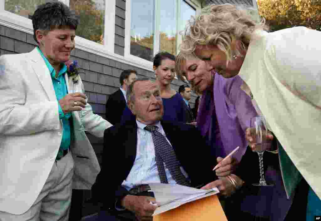 In this Sept. 21, 2013 photo, former president George H.W. Bush prepares to sign the marriage license of longtime friends Helen Thorgalsen (right) and Bonnie Clement (left) in Kennebunkport, Maine. Bush was an official witness at the same-sex wedding, his spokesman said, Sept. 25, 2013.