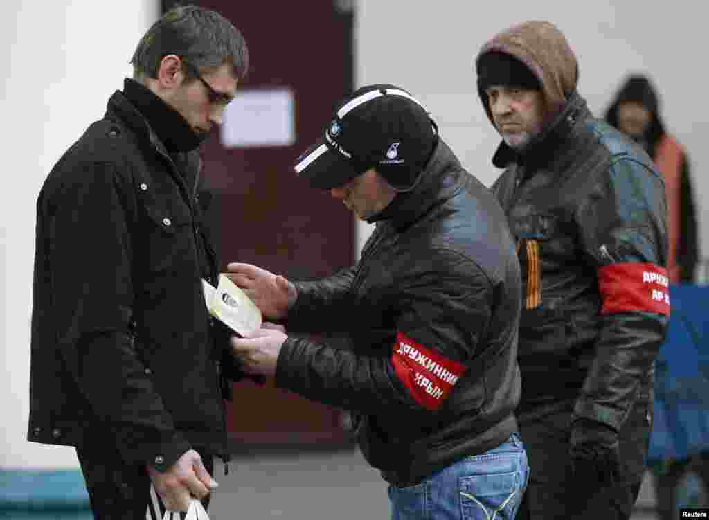 Members of a Crimean self-defence unit check the passport of a passenger at the railway station in Simferopol, Crimea, Ukraine, March 11, 2014. 