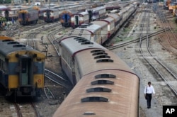 FILE - A man walks along rail tracks past moving and parked trains in Bangkok, Thailand, July 10, 2014. The military government is set to sign a more than $5 billion agreement with China for a high-speed rail network.