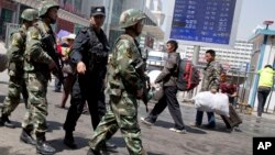 FILE - Armed Chinese paramilitary policemen march past the site of an explosion outside the Urumqi South Railway Station in Urumqi in northwest China's Xinjiang Uygur Autonomous Region, May 1, 2014.
