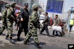 FILE - Armed Chinese paramilitary policemen march past the site of an explosion outside the Urumqi South Railway Station in Urumqi in northwest China's Xinjiang Uygur Autonomous Region, May 1, 2014.