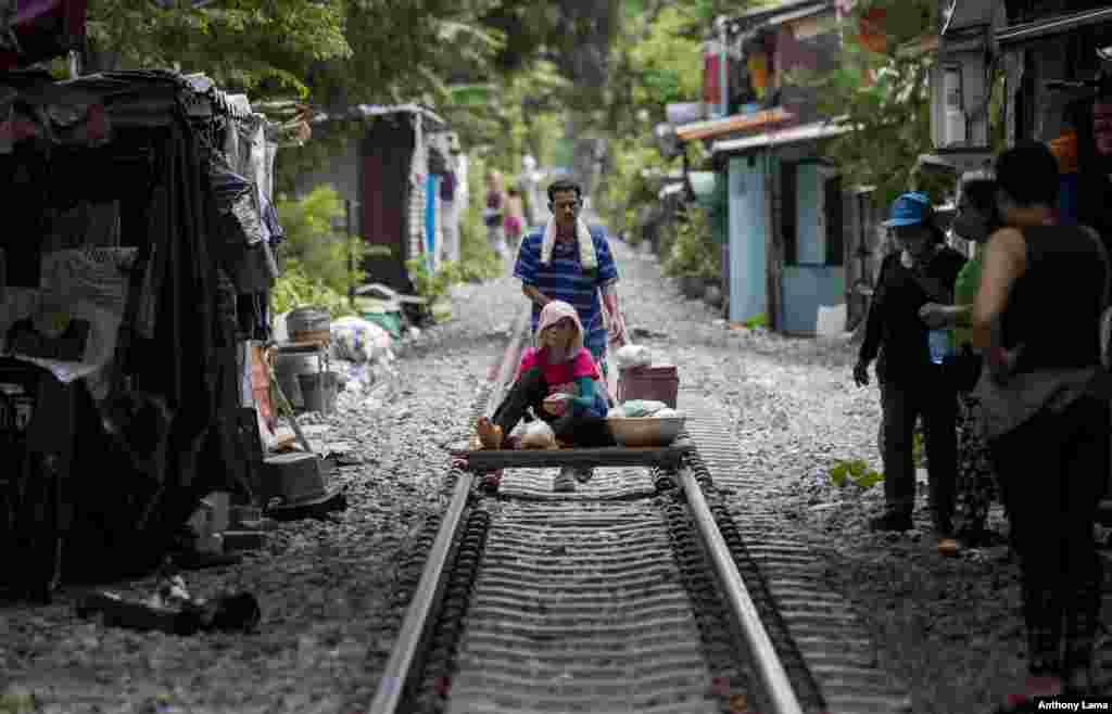 A vendor pushes a cart with a woman and merchandise along a rarely used rail track in Bangkok, Thailand.
