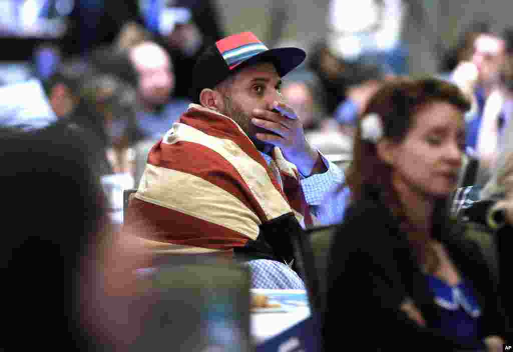 Khaled Nasr of Boston, sits wrapped in an American flag as he watches returns on a nearby large projection screen during the Dallas County Democrats watch party, Nov. 8, 2016, in Dallas. 