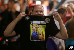 FILE - A Donald Trump supporter holds up his shirt, which bears the slogan "Build a Wall," at a campaign rally for Trump, Aug. 30, 2016, in Everett, Wash.