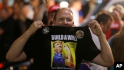 FILE - A Donald Trump supporter holds up his shirt, which bears the slogan "Build a Wall," at a campaign rally for Trump, Aug. 30, 2016, in Everett, Wash.