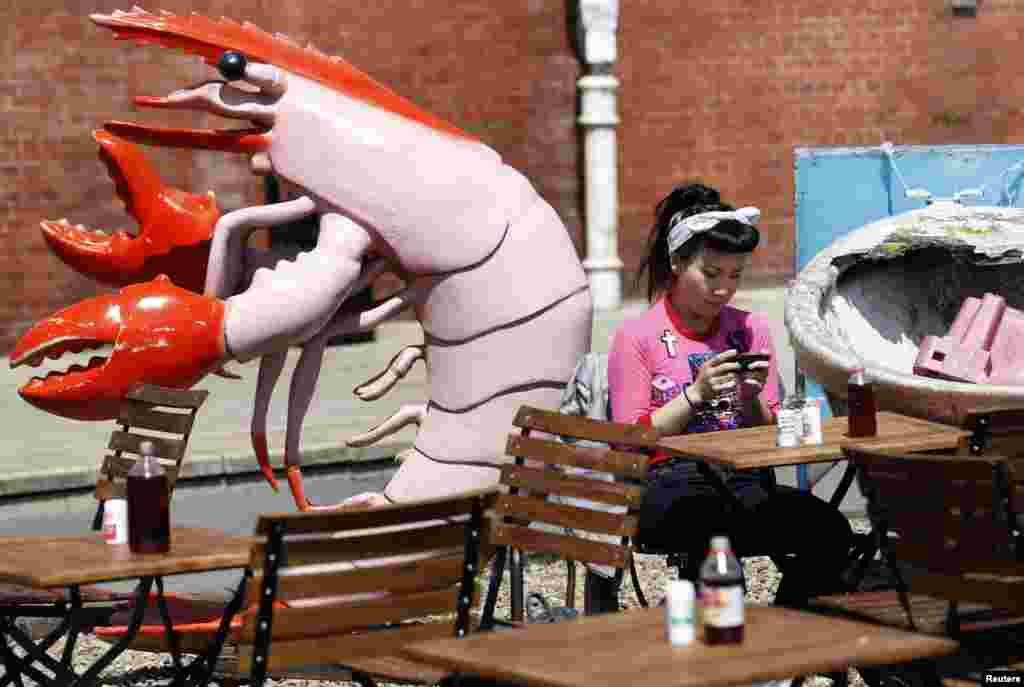 A woman sits next to a large plastic shrimp at a cafe on Brighton Beach in Brighton, southern England. 