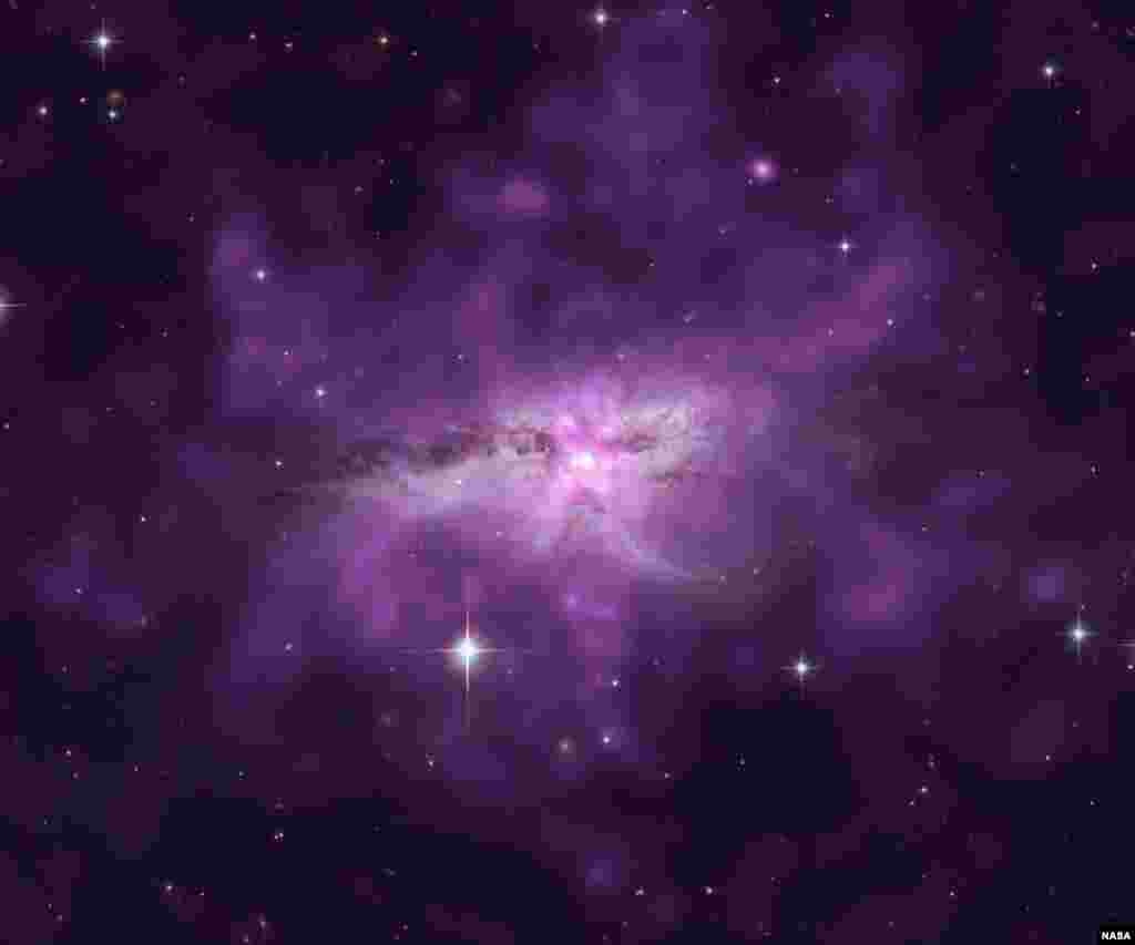 An enormous cloud of hot gas enveloping two large, colliding galaxies in the system known as NGC 6240. Scientists have used Chandra to make a detailed study of this unusually large reservoir of gas contains as much mass as 10 billion Suns, spans about 300,000 light years, radiates at a temperature of more than 7 million degrees, and glows in X-rays (purple).