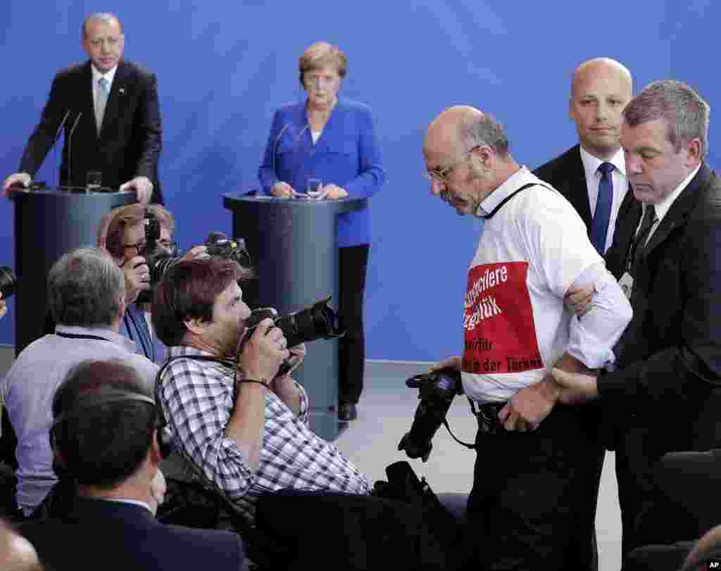 A protester is taken away as Turkish President Recep Tayyip Erdogan and German Chancellor Angela Merkel, right, give a joint press conference in Berlin.