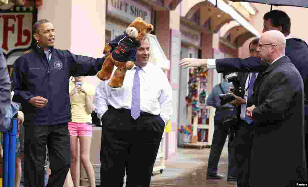 바락 오바마 미국 대통령(왼쪽)이 28일 뉴저지주 크리스 크리스티 주지사와 함께 지난해 허리케인 샌디 피해 복구 지역인 해안가 마을 포인트플레즌트를 방문했다. 오바마 대통령이 거리 매대에서 게임을 하고 상품으로 받은 곰 인형을 들어보이고 있다.