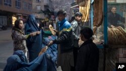 A man distributes bread to Burka-wearing Afghan women outside a bakery in Kabul, Afghanistan, Dec, 2, 2021.