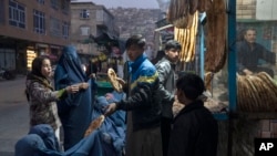 A man distributes bread to Burka-wearing Afghan women outside a bakery in Kabul, Afghanistan, Dec, 2, 2021.