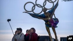 Visitors pose for a selfie with a statue containing the Olympic rings at a park near the headquarters for the Beijing Organizing Committee for the Olympic Games in Beijing, Dec. 16, 2021