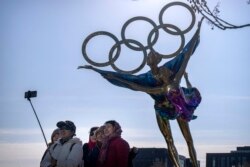 Pengunjung berfoto selfie dengan patung berisi cincin Olimpiade di taman dekat markas besar Panitia Penyelenggara Olimpiade Beijing di Beijing, 16 Desember 2021. (Foto: AP)