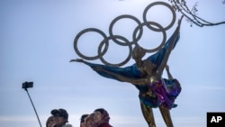 Du khách chụp ảnh trước bức tượng có các vòng tròn Olympic tại một công viên gần trụ sở của Ban tổ chức Thế vận hội Olympic ở Bắc Kinh, ngày 16/12/2021 (AP Photo/Mark Schiefelbein).