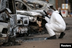 A French police officer photographs burned vehicles outside the Splendid Hotel in Ouagadougou, Burkina Faso, Jan. 17, 2016.