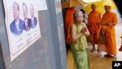 A Cambodian People's Party poster hangs on a wall outside a business as a woman offers prayers to Buddhist Monks, file photo. 