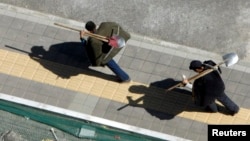 資料照：北京國家體育館附近兩名打工人扛著鐵鍬鋤頭去上工。