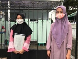 Gunita Sri (kiri) dan sepupunya yang juga relawan Riani Wulandari (kanan) berdiri dengan jarak fisik usai mengikuti penyuntikkan vaksin dalam uji klinis tahap 3 di Puskesmas Dago, Bandung, Jumat (14/8) siang. (VOA/Rio Tuasikal)