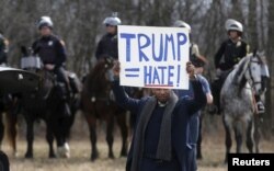 FILE - An anti-Trump protester holds a protest sign in front of mounted police outside a rally for then Republican U.S. presidential candidate Donald Trump in Cleveland, Ohio, March 12, 2016. Minorities have been especially concerned about whether Trump's xenophobic rhetoric will translate into policy.