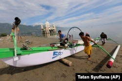 In this April 3, 2019, photo, local fishermen pull a boat to the beach as a mosque heavily damaged by the 2018 earthquake and tsunami is seen in the background in Palu, Central Sulawesi, Indonesia.