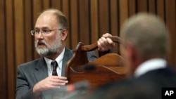 Forensic expert, Roger Dixon, left, holds a court exhibit, a magazine rack, as he answers questions put to him by chief state prosecutor Gerrie Nel , right, during the murder trial of Oscar Pistorius, in Pretoria, South Africa, April 17, 2014. 