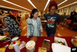 Miaofan Chen, left, works her way through the dessert choices along with Thandi Glick during a potluck meal for Chinese exchange students and their host families in Denver, Jan. 27, 2017.