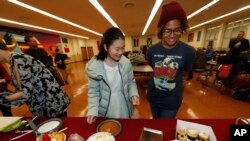 FILE - Miaofan Chen, left, works her way through the dessert choices along with Thandi Glick during a potluck meal for Chinese exchange students and their host families in Denver, Jan. 27, 2017.