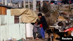 FILE - A woman and her daughter stand outside their shack in a slum of Villa Fiorito, on the outskirts of Buenos Aires, Argentina, June 15, 2016.