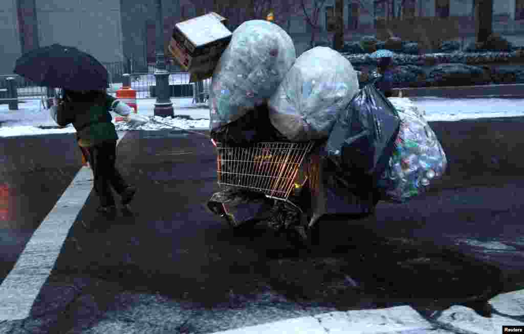A woman pulls a cart loaded with plastic bottles through falling snow in lower Manhattan in New York City. A winter storm pushed into the northeast U.S. with several inches of snow forecasted for the New York City area.