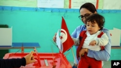 FILE - A woman casts her vote with her child during the first round of the Tunisian presidential election in a polling station at Marsa, outside Tunis, Nov. 23, 2014. The vote was another step forward in Tunisia's peaceful transition to democracy.