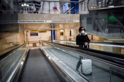 A woman wears a mask as she stands on an escalator inside Central train station, in Milan, Italy, Sunday, March 8, 2020.