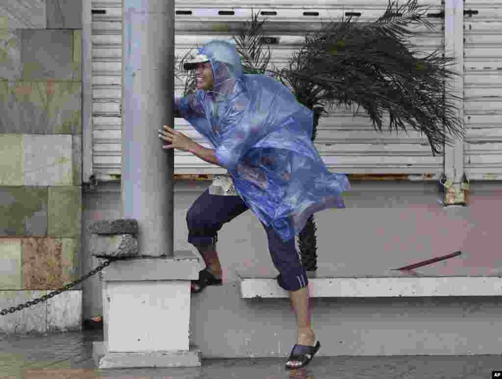 A man holds on to a pole as strong winds brought by Typhoon Hagupit blow in Legazpi, Albay province, eastern Philippines.Typhoon Hagupit slammed into the central Philippines' east coast, knocking out power and toppling trees in a region where 650,000 people have fled to safety.