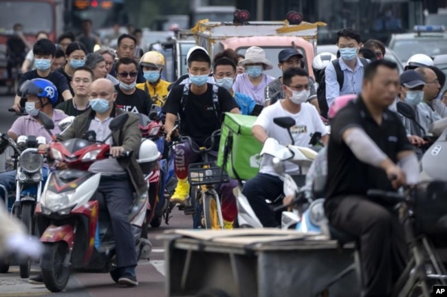 FILE - In this file photo dated Friday, July 2, 2021, people riding bicycles and scooters wait to cross an intersection during rush hour in Beijing. (AP Photo/Mark Schiefelbein, FILE)