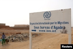 FILE - A boy walks past a signboard for the International Migration Organization's transit center in Agadez, Niger, May 11, 2016.