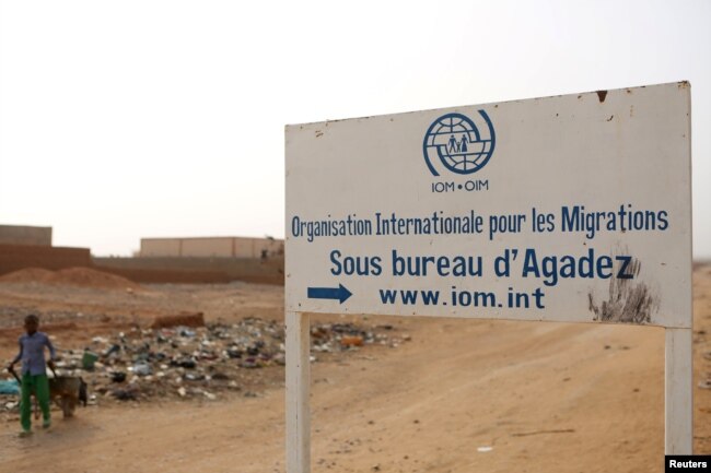FILE - A boy walks past a signboard for the International Migration Organization's transit center in Agadez, Niger, May 11, 2016.