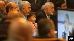 Yehiya Sinwar, left, a top Hamas official in Gaza, holds his son's Ibrahim, while sitting near Ismail Haniyeh, right, a former top Hamas official in Gaza, while listening to Khaled Mashaal, the outgoing Hamas leader in exile, during his news conference in Doha, Qatar, while display on a screen in Gaza City, May 1, 2017. Hamas unveiled what had been billed as a new, seemingly more pragmatic political program. 