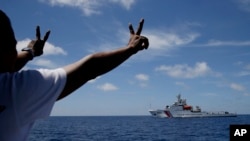 FILE - Philippine crewmen gestures toward a Chinese Coast Guard ship as they block them from entering Second Thomas Shoal in the South China Sea, March 29, 2014.
