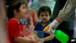 Petugas menyemprotkan disinfektan ke tangan anak-anak di sebuah toko pakaian, ketika pemerintah mulai melonggarkan pembatasan Covid-19 di Rawalpindi, Pakistan. 