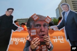 A protester wearing a mask of U.S. President Donald Trump, center, performs with cut-out photos of North Korean leader Kim Jong Un and South Korean President Moon Jae-in, right, during a rally against the United States' policies.